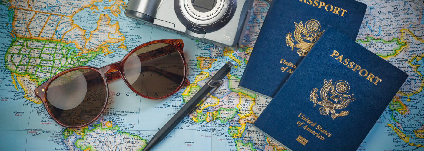 Passports, a camera, sunglasses, and a pen resting on top of a world map