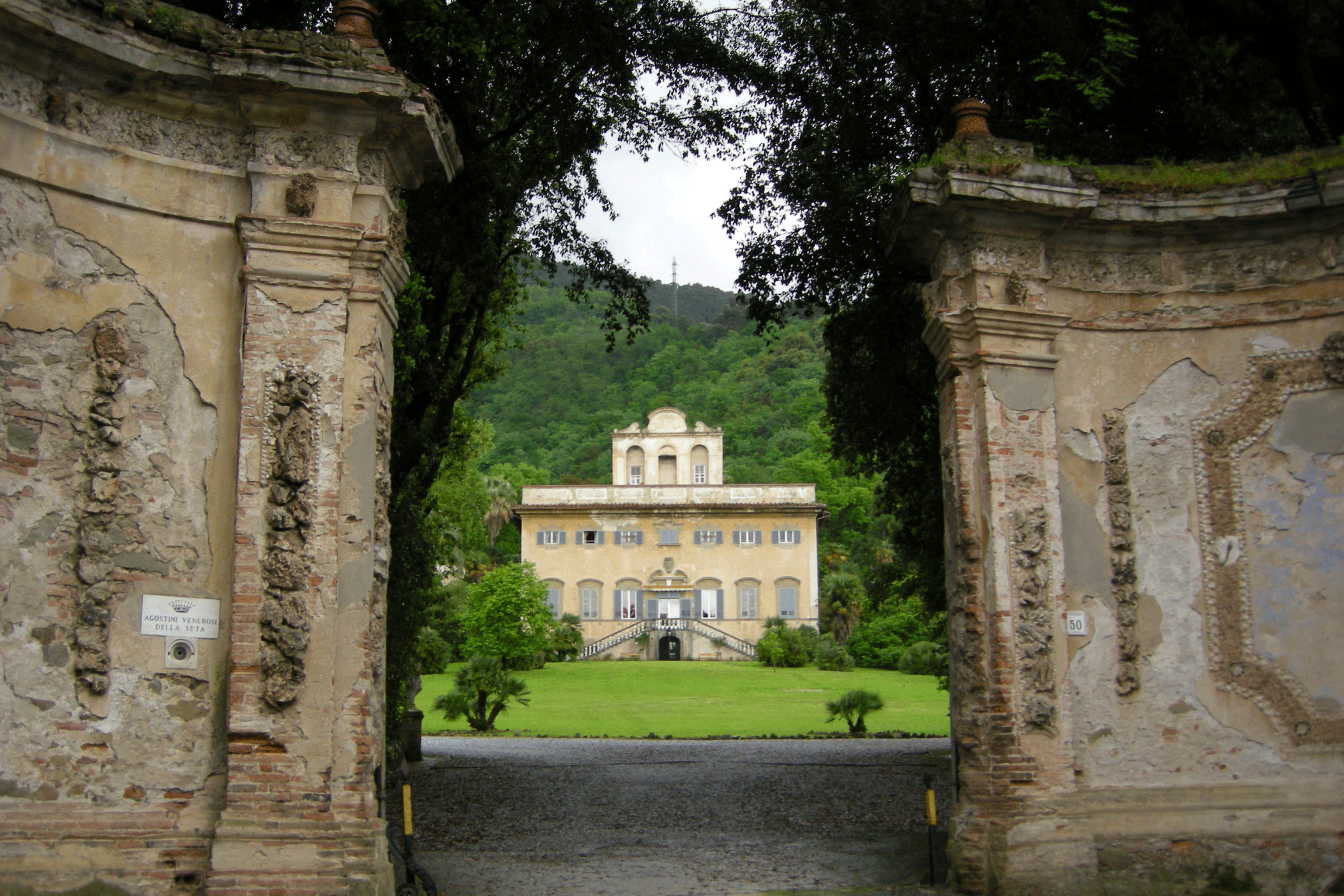 Exterior of the Villa di Corliano as seen through a gate in a large stone wall
